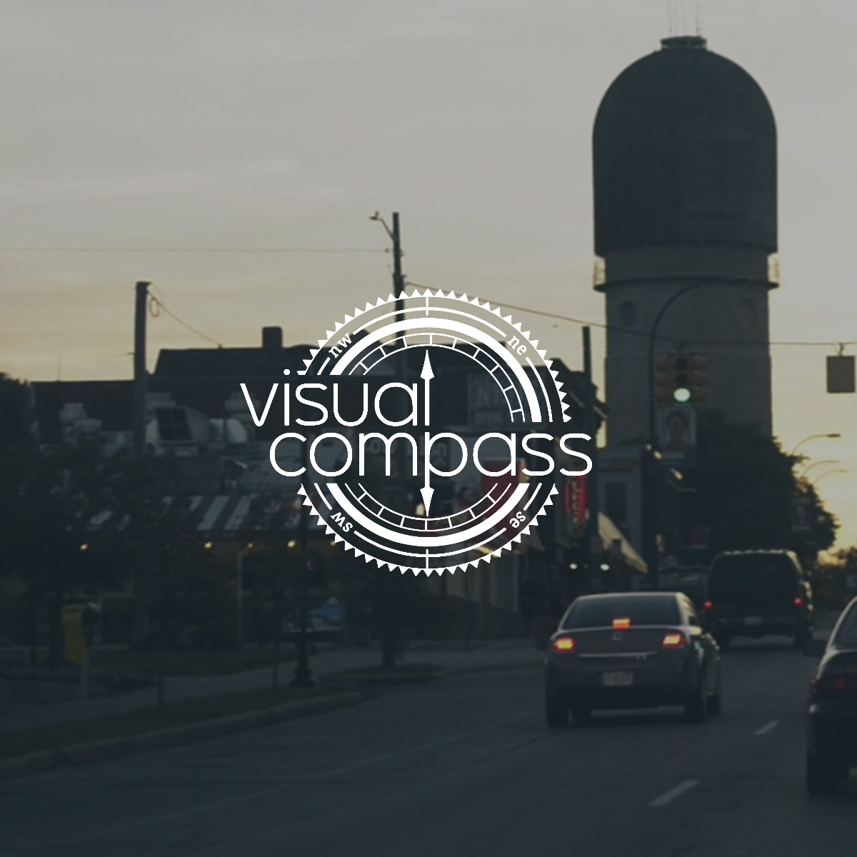 Cars on road in front of Ypsilanti's water tower with a logo of Visual Compass over the center